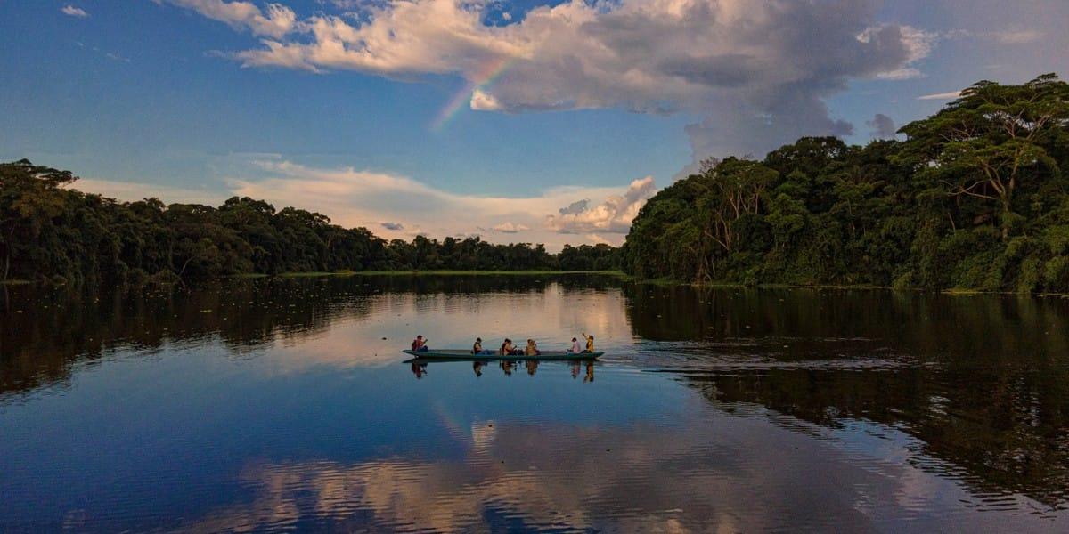 Canoe with people on Amazon River reflecting forest and clouds