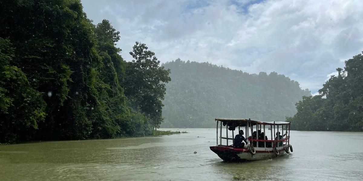 Boat with passengers navigating through rainforest river surrounded by trees